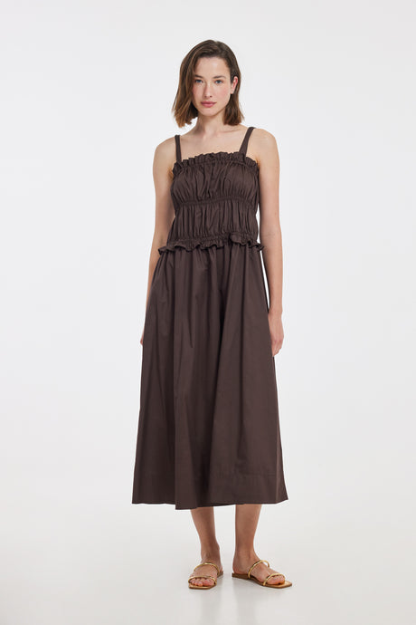 Brown sleeveless midi dress with smocked bodice and thin shoulder straps, worn with flat sandals.