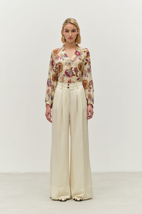 Sheer blouse with colorful floral print, buttoned cuffs, paired with high-waist wide-leg cream trousers.