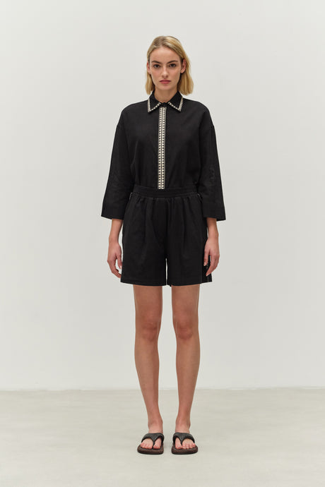 Black collared romper with 3/4 sleeves, contrasting front placket, and relaxed fit shorts.