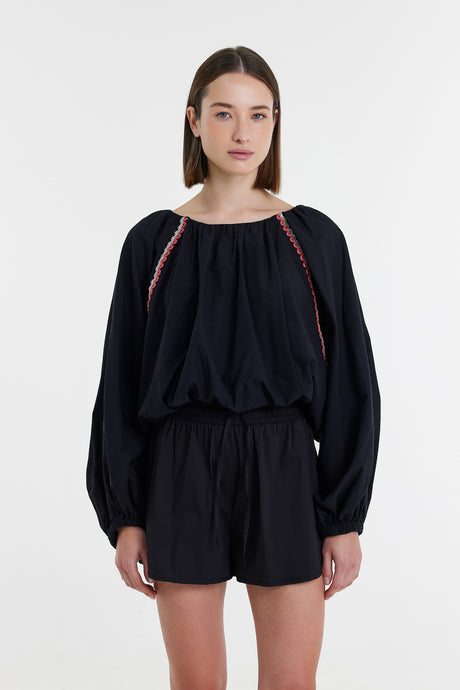 Black long-sleeve blouse with loose fit and subtle red stitching on shoulders, paired with matching black shorts.