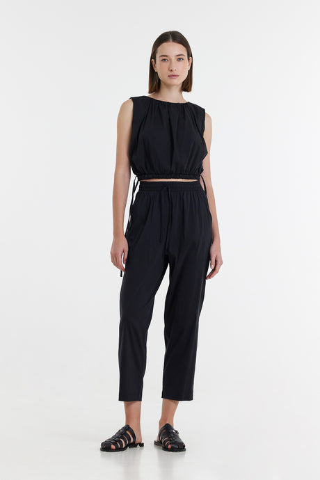 Black sleeveless cropped top with matching high-waisted tapered pants and black sandals.