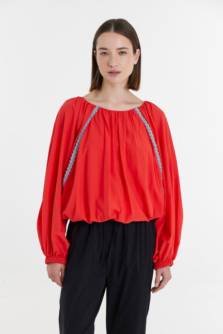 Red long-sleeve blouse with gathered neckline and black embroidered side details.