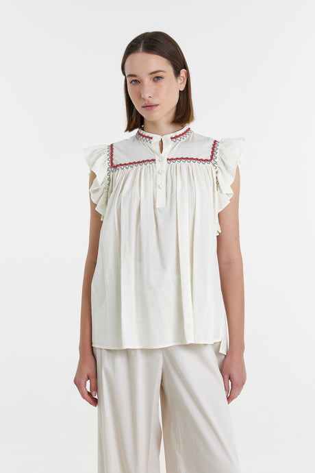 Off-white sleeveless blouse with ruffled shoulders and red embroidery near the collar and front placket.