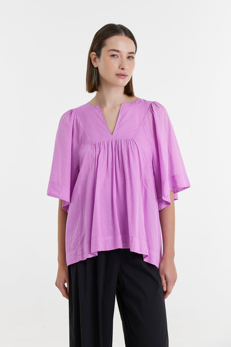 Lilac loose-fit blouse with V-neck and wide elbow-length sleeves, paired with black pants.