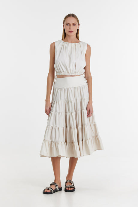 Off-white sleeveless crop top and tiered midi skirt set with ruched detailing and black sandals.