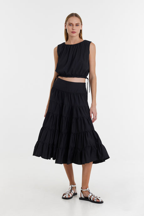 Black sleeveless crop top with side ties paired with a black tiered midi skirt and silver braided sandals.