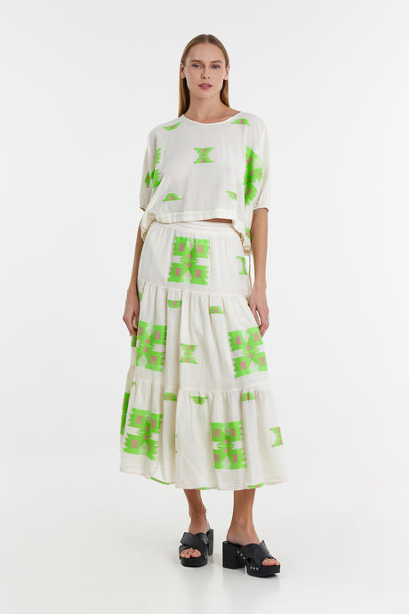 White cotton blouse and tiered midi skirt with bright green geometric jacquard patterns, paired with black platform sandals.