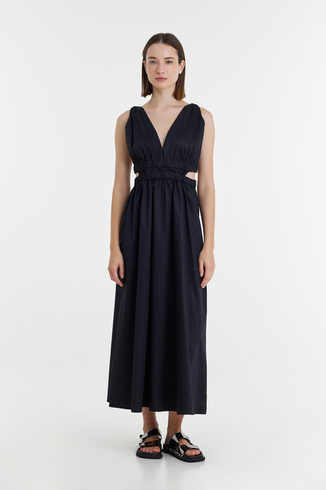 Sleeveless black maxi dress with V-neck and gathered waist, paired with black sandals.