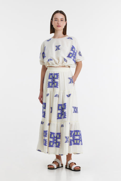 White maxi skirt with blue geometric jacquard patterns, worn with matching top and belt.