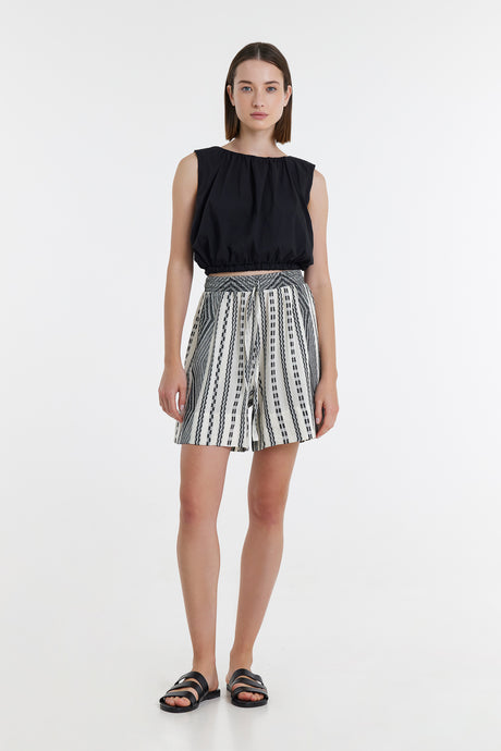 Black sleeveless top paired with black and off-white jacquard patterned high-waist shorts and black slide sandals.