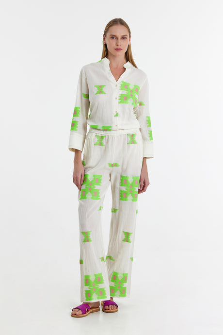 White wide-leg pants and matching button-up shirt with lime green geometric print, worn with purple sandals.