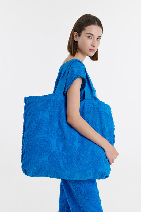 Bright blue oversized tote bag with textured floral pattern and short handles.