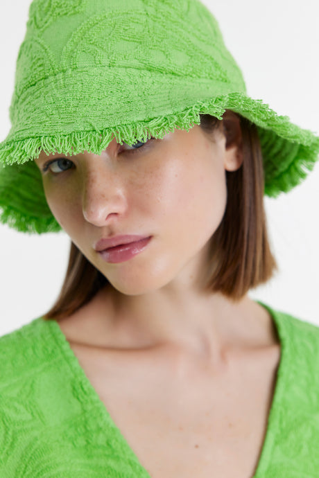 Bright green textured terry cloth bucket hat with frayed edges worn by model.