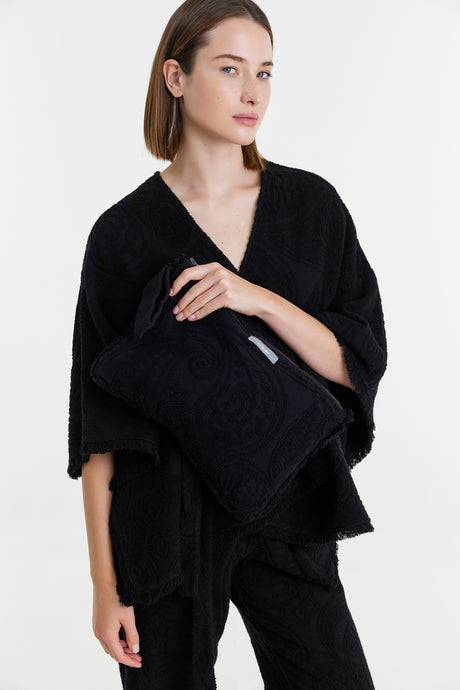 Black textured clutch bag held by woman wearing loose black knitwear and matching pants.
