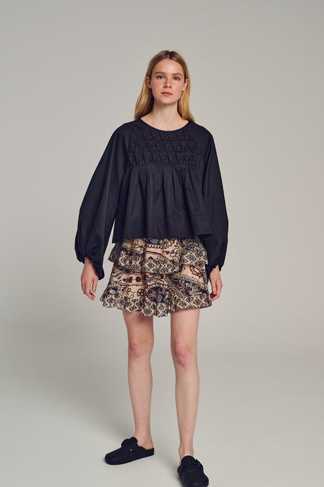 Black long-sleeve Crete blouse with gathered yoke and loose fit worn with leopard print ruffle mini skirt.