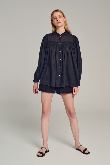 Black long-sleeve button-up blouse with gathered yoke and loose fit on model.