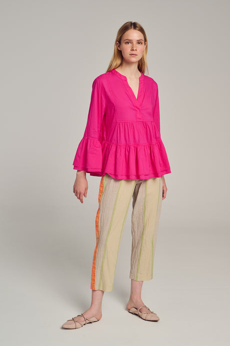 Bright pink blouse with V-neck and tiered bell sleeves paired with beige pants with red and yellow side stripes.