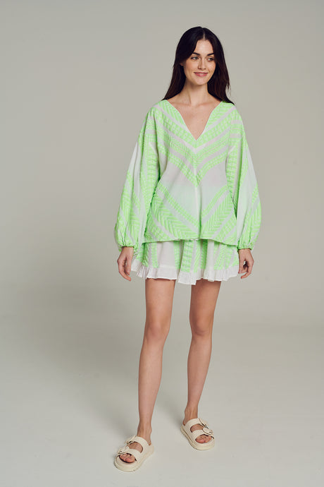 Light green and white jacquard blouse with billowy sleeves and V-neck worn with white shorts.