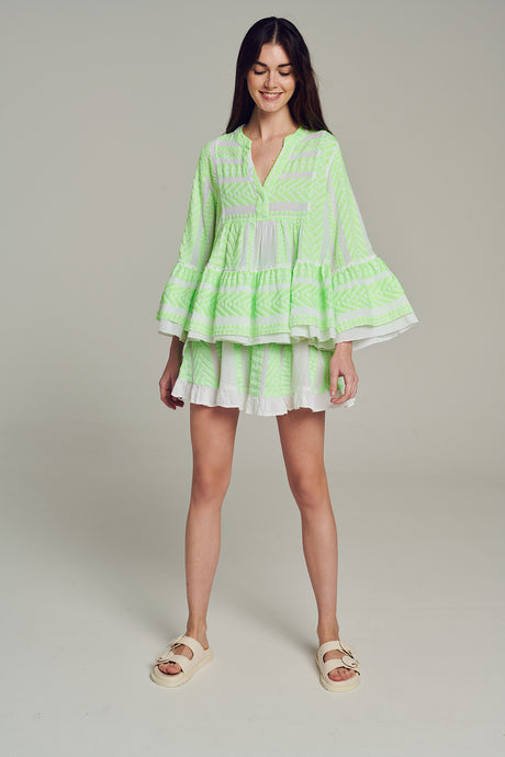 Green jacquard blouse with tiered ruffle hem and wide bell sleeves worn with white shorts.