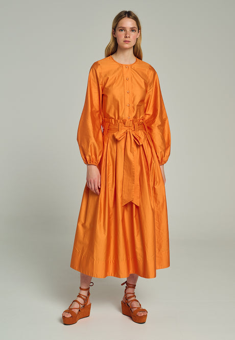 Orange midi dress with long puffed sleeves and a cinched waist tie, paired with brown strappy sandals.