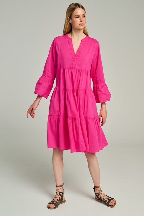 Bright pink midi dress with tiered skirt, long puff sleeves, and V-neckline, worn with black lace-up sandals.