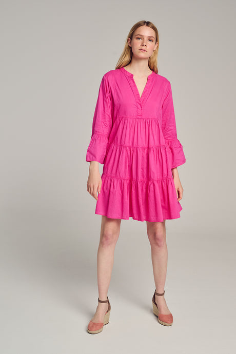 Bright pink tiered mini dress with long puff sleeves and V-neckline worn with beige wedge sandals.