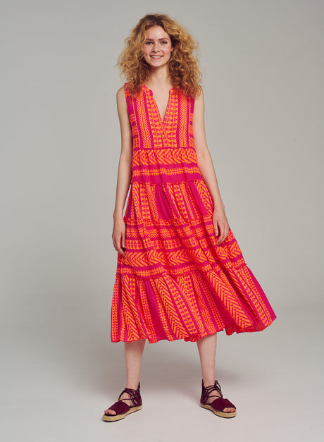 Sleeveless midi dress with deep V-neck, jacquard pattern in vibrant neon orange and fuchsia, flowing skirt, worn with flat.