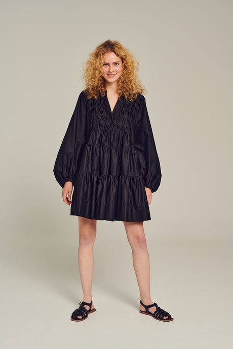 Black short dress with long puff sleeves and tiered skirt worn with flat black sandals.
