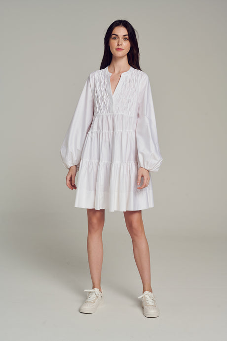 White long-sleeve mini dress with tiered skirt and delicate front pintuck details.