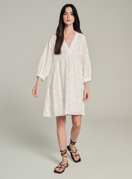 White knee-length dress with long sleeves, V-neck, and delicate embroidered pattern.