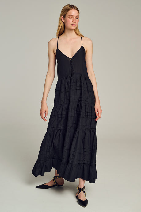 Black sleeveless maxi dress with tiered skirt and thin adjustable straps worn with black lace-up flats.