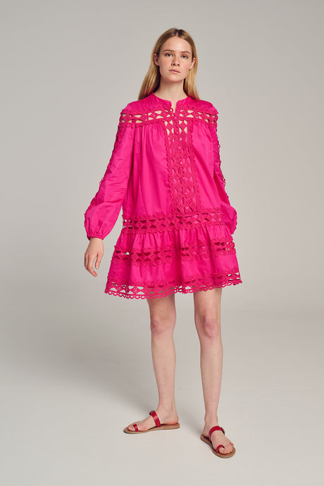 Pink long-sleeve short dress with lace cutouts and tiered skirt, worn with flat sandals.