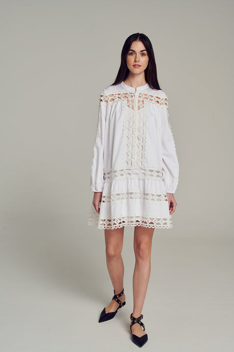 White off-shoulder short dress with lace panels and long sleeves, worn with black ankle-wrap flats.