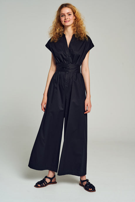 Black wide-leg jumpsuit with short sleeves and a belted waist, styled with black sandals.