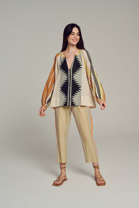 Woman wearing multicolor jacquard knit cardigan with geometric pattern and beige cropped pants with red and black vertical.