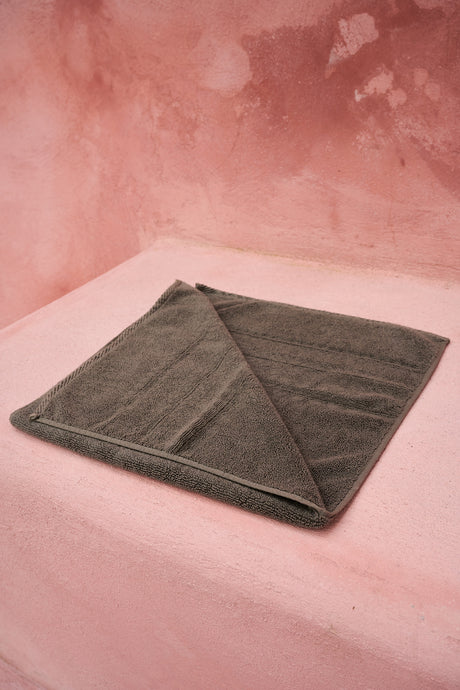 Folded small grey bath towel with a soft, plush texture on a pink surface.