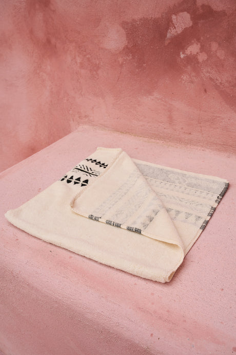 Folded black and off-white bath towel with geometric patterns on a pink surface.
