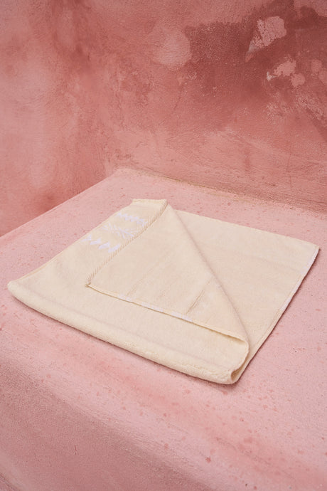 Soft off-white bath towel folded neatly on a pink surface with a corner turned over.