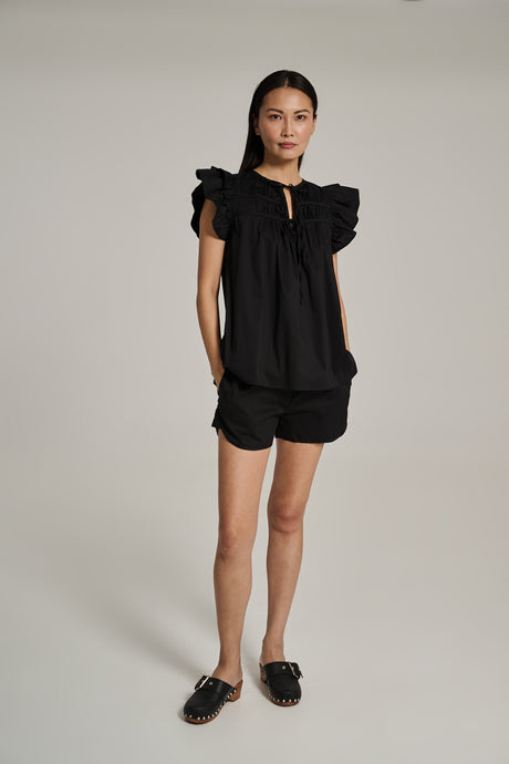 Black sleeveless popeline top with ruffled shoulders and keyhole neckline paired with black shorts.