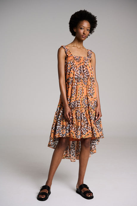 Orange midi dress with abstract print, sleeveless design, ruffled hem, worn with black sandals.