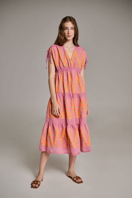 Midi dress in pink and orange jacquard with tiered skirt and short sleeves, worn with brown sandals.
