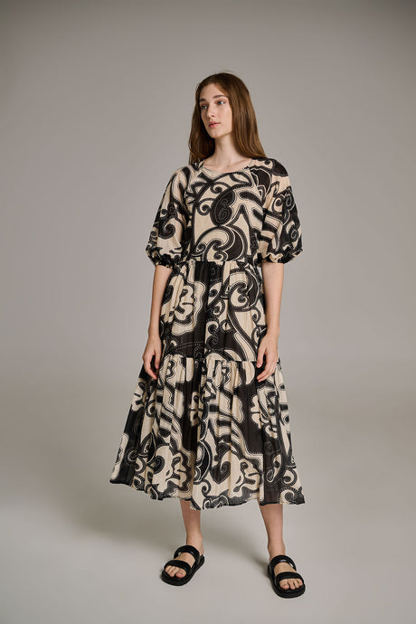 Black and off-white long dress with bold abstract print and tiered skirt, paired with black sandals.