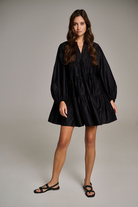 Black short dress with voluminous long sleeves and tiered skirt, paired with black sandals.