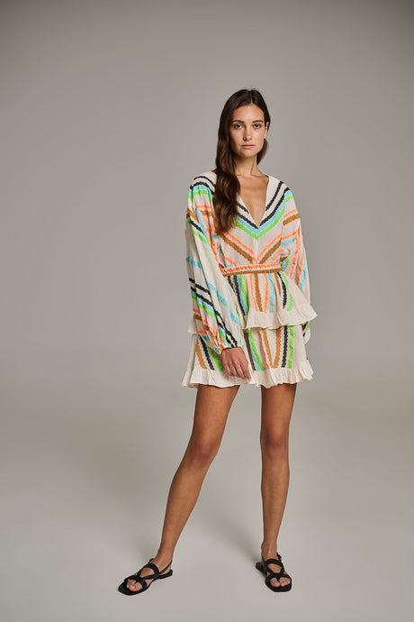 Off-white blouse with colorful jacquard stripes, V-neck, long sleeves, and ruffled hem worn with shorts.