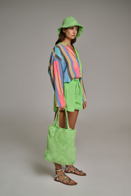 Woman wearing neon green bucket hat and matching terry cloth shorts with a multicolor striped blouse, carrying a lime green.