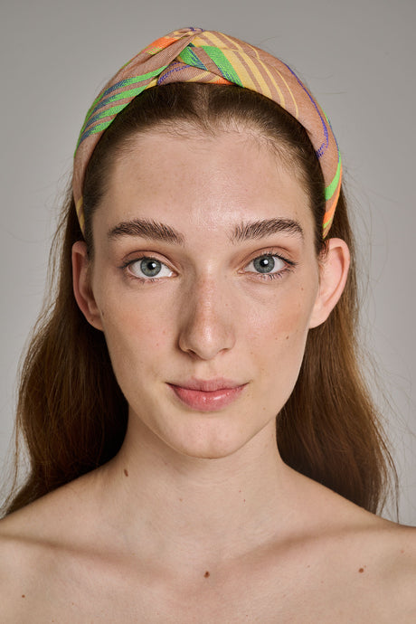 Beige and orange striped fabric hairband twisted at the top worn by a woman with straight brown hair.