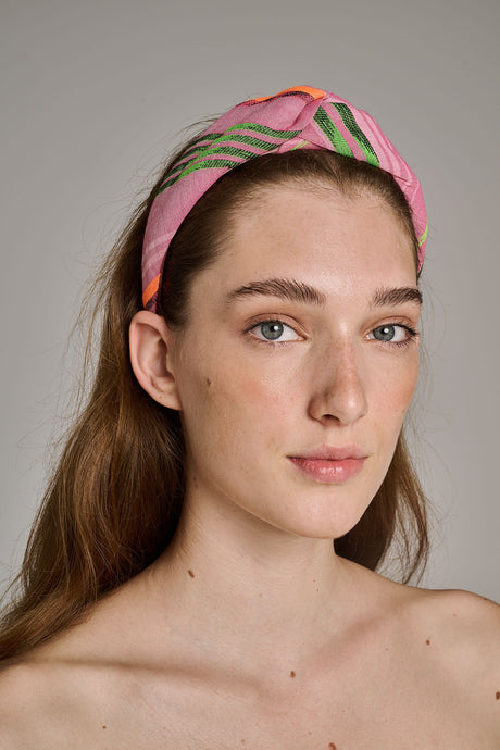 Pink and orange striped fabric hairband with a twisted knot detail worn by a woman.