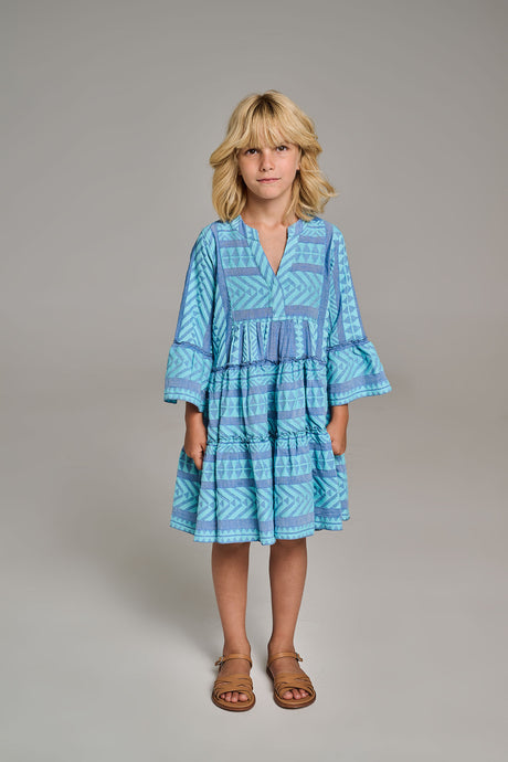 Blue patterned long-sleeve tiered mini dress with v-neck and ruffled cuffs worn by girl.