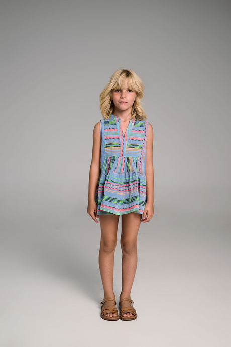 Blue sleeveless romper with pink and green tribal patterns worn by girl with sandals.